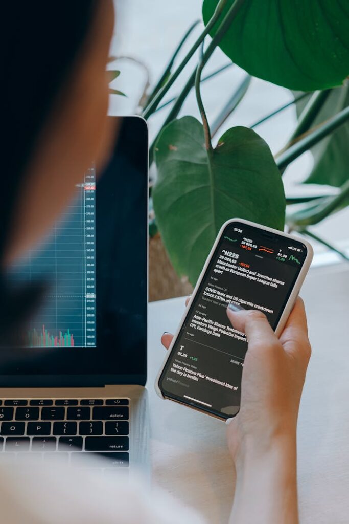 Person multitasking with financial graphs on laptop and smartphone, perfect for business concepts.