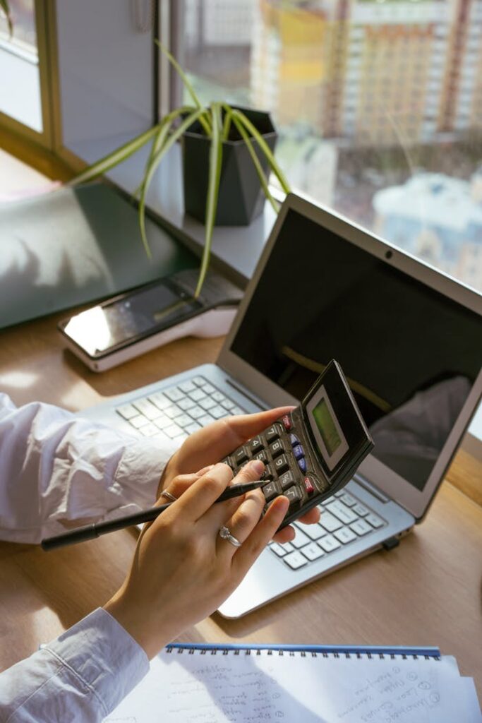 Person calculating at desk with laptop and notebook. Ideal for business and finance themes.